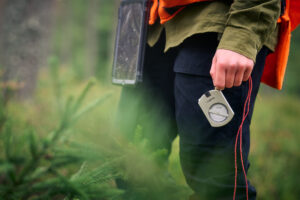 Mies työskentelee metsässä ja kartoittaa sitä kompassi kädessään kuusen taimien takana